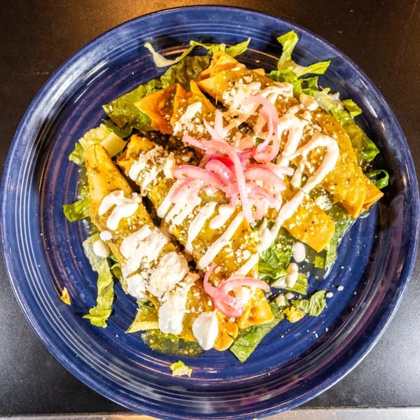 A blue plate of enchiladas verdes topped with lettuce, sour cream, cheese, and pickled red onions.