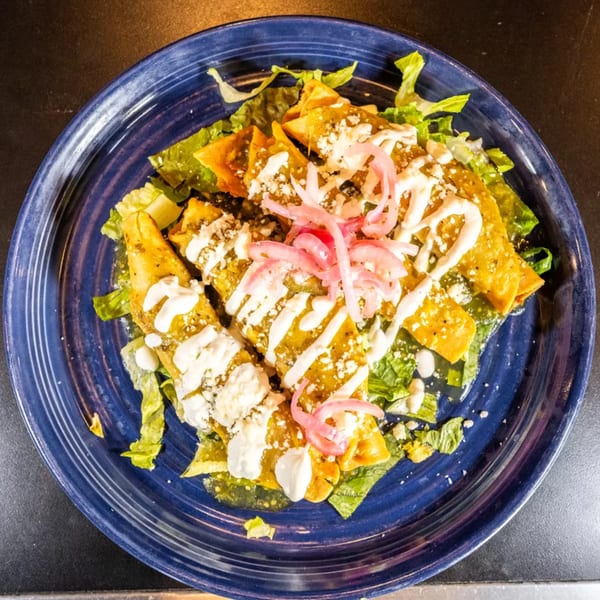 Chilaquiles with green salsa, sour cream, cheese, and pickled red onions on a blue plate.