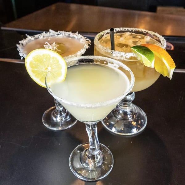 Three margaritas with salt rims and citrus garnishes on a dark bar top.