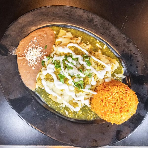 Enchiladas with green sauce, sour cream, cilantro, onions, refried beans, and orange rice.
