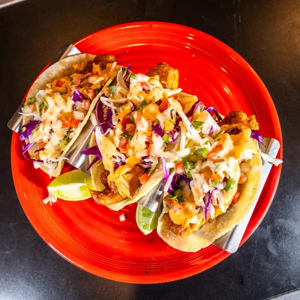 Three fish tacos with cabbage, salsa, and sauce, served on a vibrant red plate.