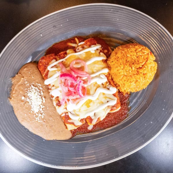 Enchiladas with red sauce, melted cheese, pickled onions, refried beans, and orange rice.